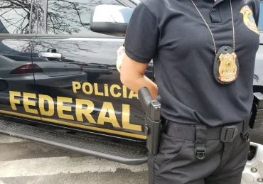 Fotografia de um policial parado ao lado de uma viatura